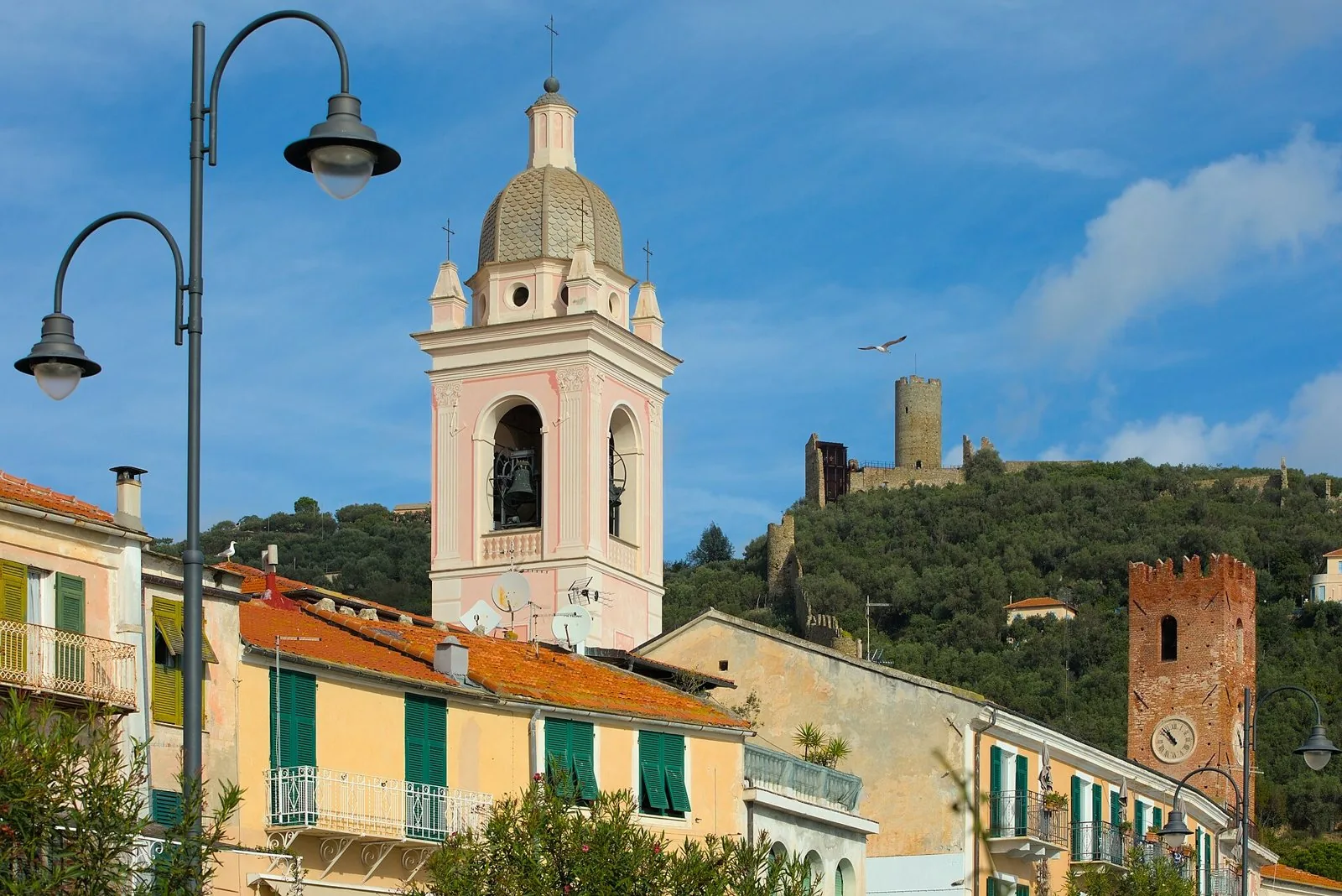 Il campanile rosa della cattedrale di San Pietro e la Torre del Comune nel centro storico di Noli, con il castello sulla collina