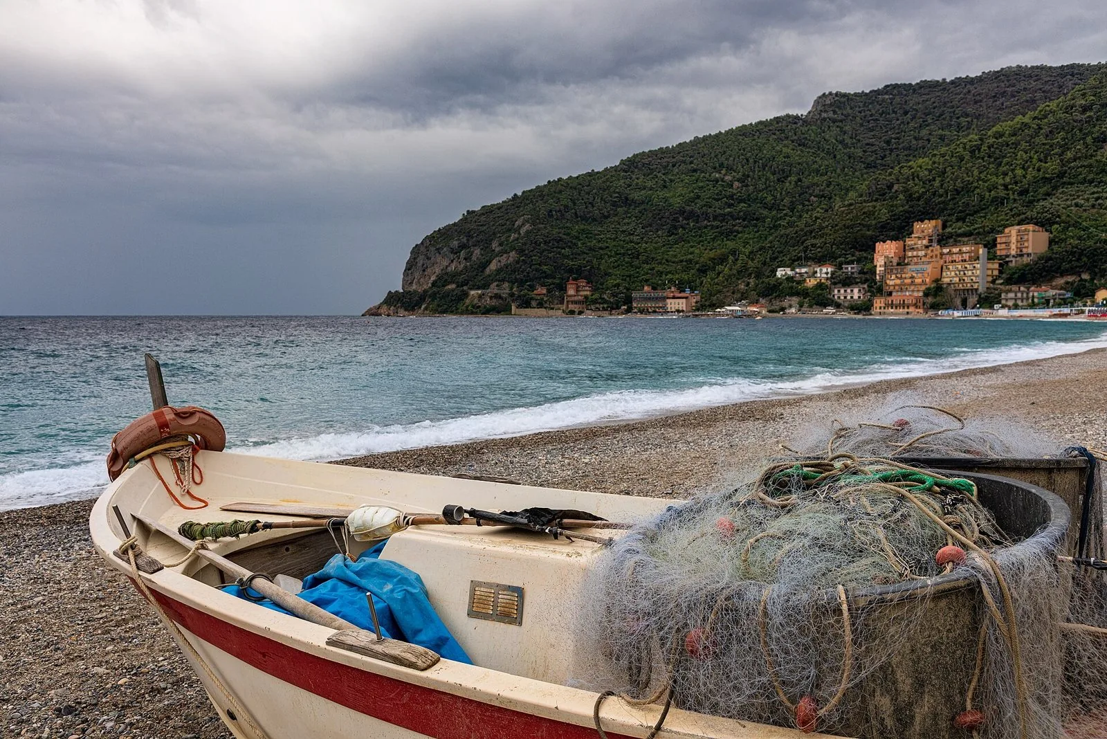 Barca da pesca con le reti sulla spiaggia di ciottoli di Noli, con il promontorio sullo sfondo
